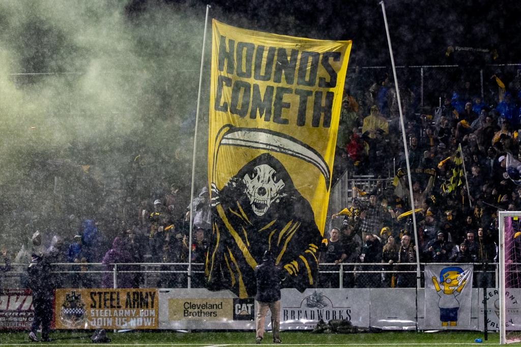 Picture of Pittsburgh Riverhounds supporter section, the steel army, holding up a banner during a game at Highmark Stadium. 
