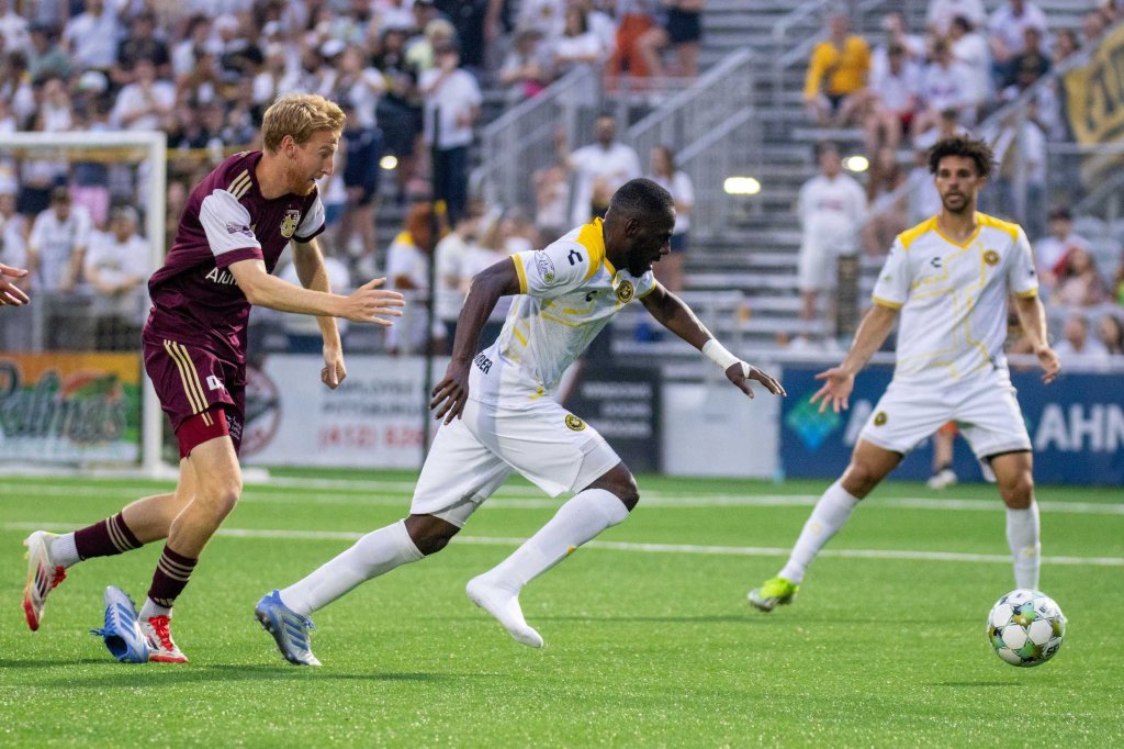 Junior Etou escapes the grasp of Detroit City FC's Connor Rutz — and one of his own boots — in the Riverhounds' 2-0 win on June 7, 2025 at Highmark Stadium in Pittsburgh. (Photo: Chris Cowger/Riverhounds SC)