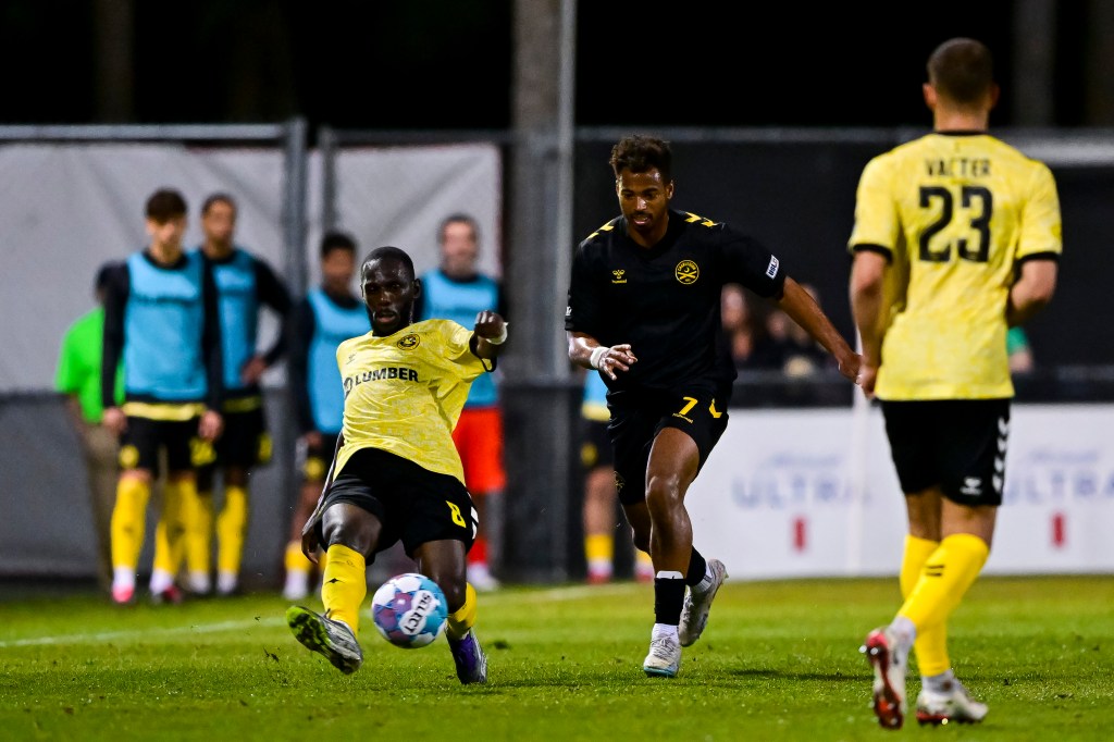 Pittsburgh Riverhounds wing back Junior Etou lunges to play the ball ahead of the Charleston Battery's Langston Blackstock in the teams' match March 7, 2026 at Patriots Point Soccer Complex in Mount Pleasant, S.C. (Photo: Charleston Battery)