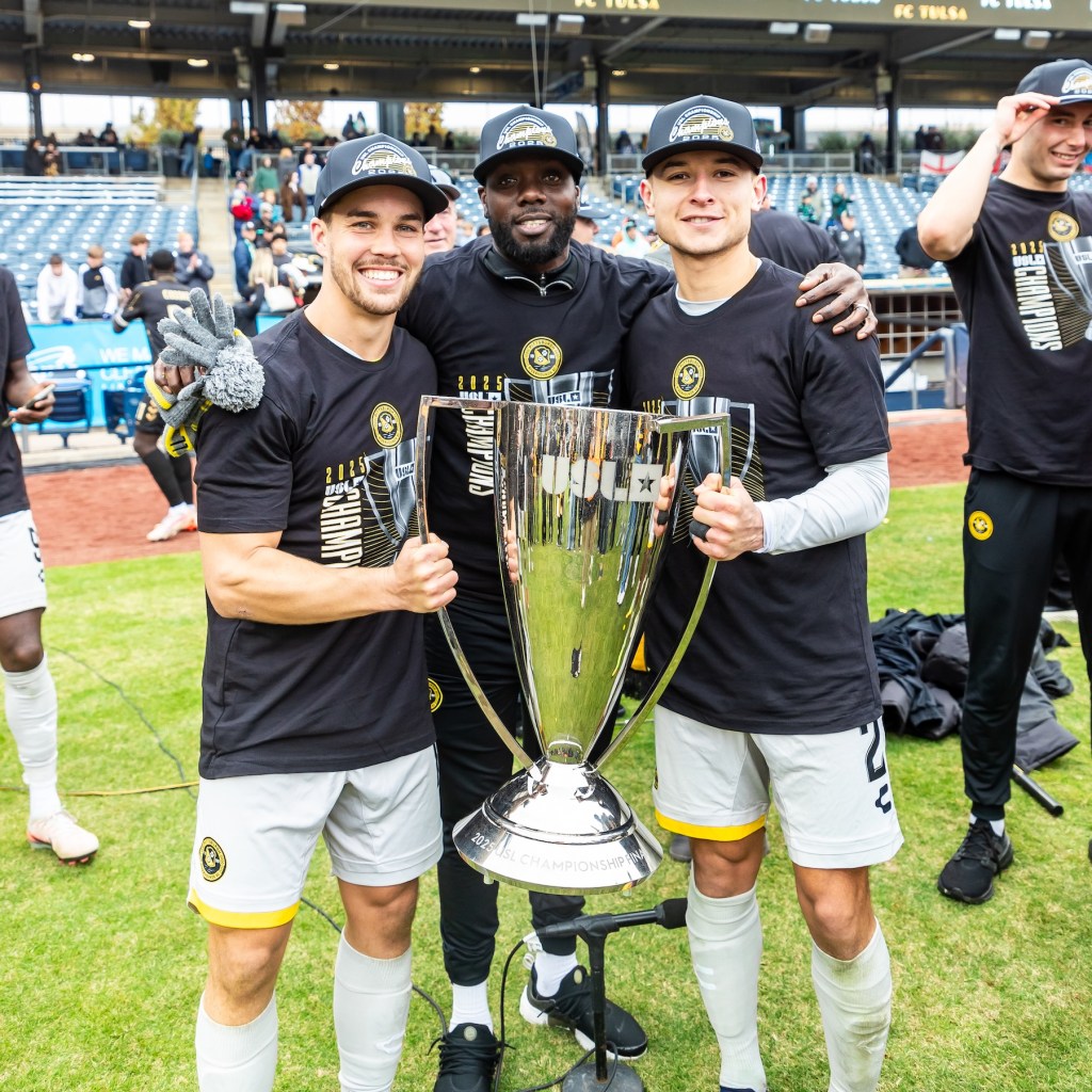 The members of the Pittsburgh Riverhounds' 200 appearance club — Robbie Mertz, Kenardo Forbes and Danny Griffin — smile while holding the USL Championship Trophy on Nov. 22, 2025 after the Hounds' victory in the Final at ONEOK Field in Tulsa, Okla. (Photo: Mallory Neil/Riverhounds SC)